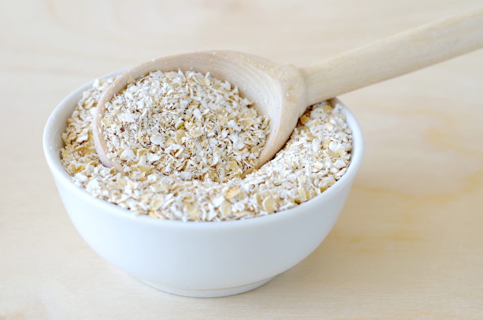 Oat bran in bowl with spoon on wooden background