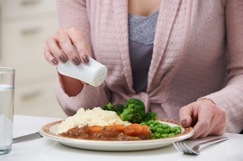 Woman At Home Adding Salt To Meal